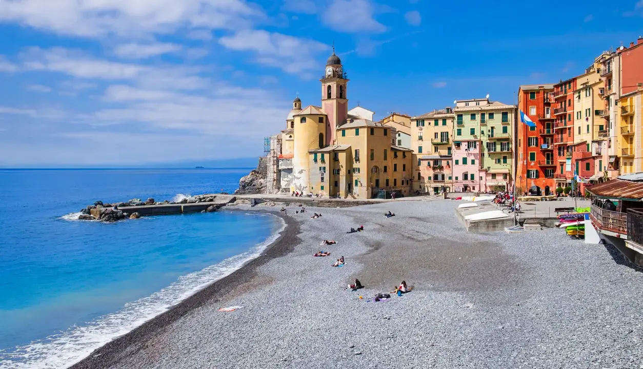 Un mare bello in Liguria, con la spiaggia di ciottoli e le case colorate di Camogli che si affacciano sull'acqua azzurra.
