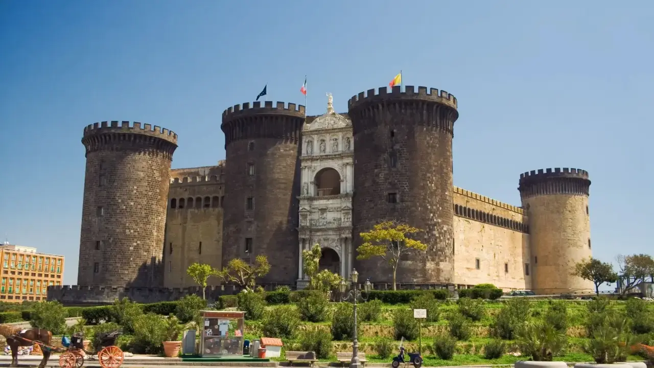 Il maestoso Maschio Angioino di Napoli, con le sue torri imponenti e l'arco trionfale, si staglia contro il cielo azzurro.