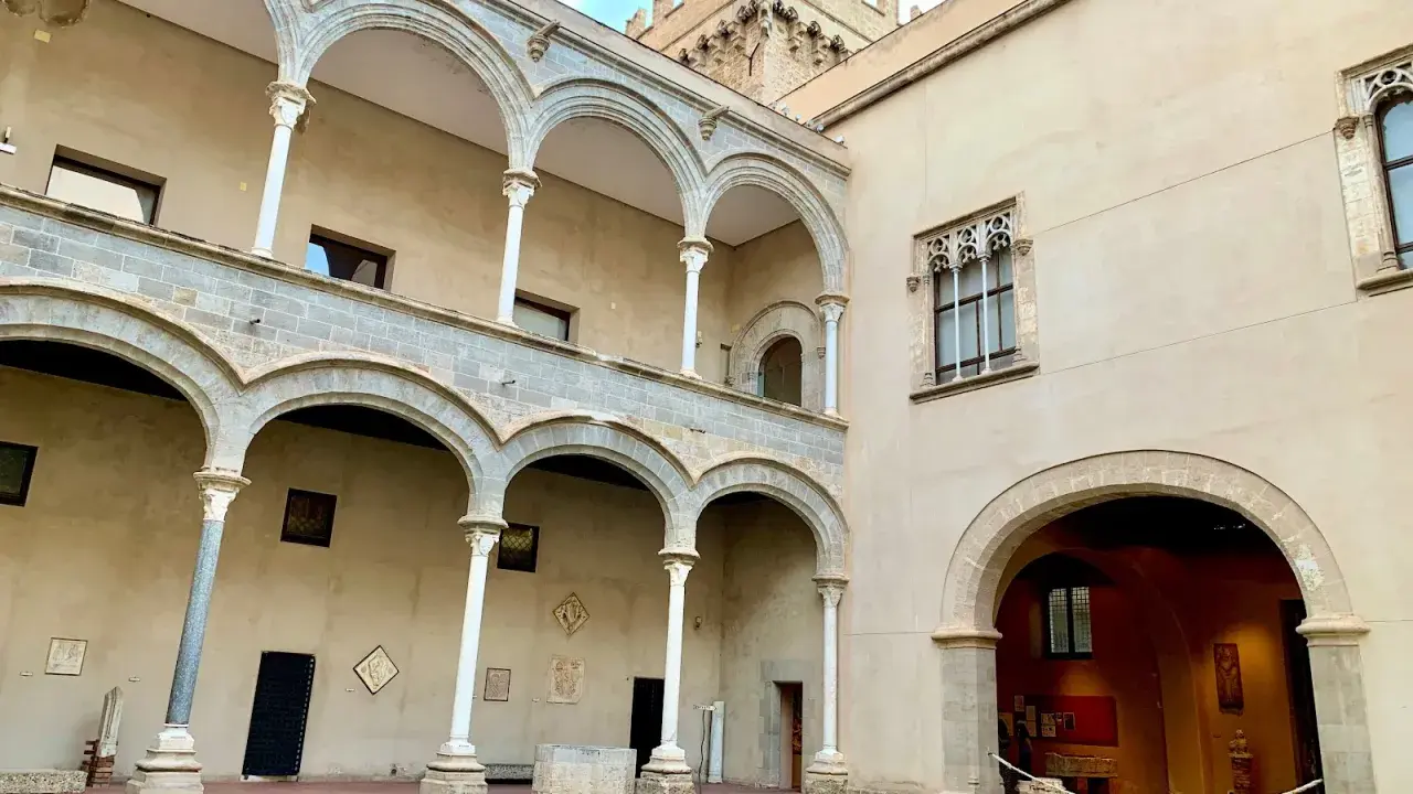 Cortile di Palazzo Abatellis, con arcate sovrapposte, finestre gotiche e opere d'arte esposte.