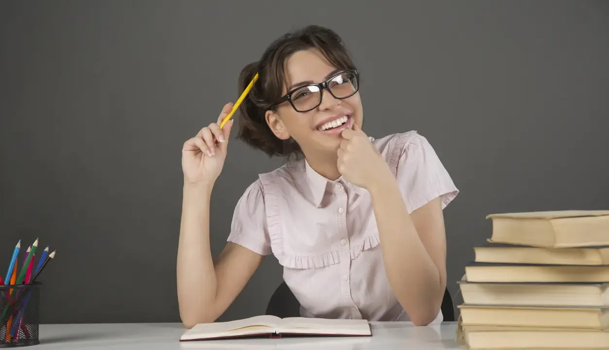 Ragazza con occhiali e matita gialla, un libro aperto e pile di libri, un'espressione pensierosa che ricorda l'anastrofe figura retorica.