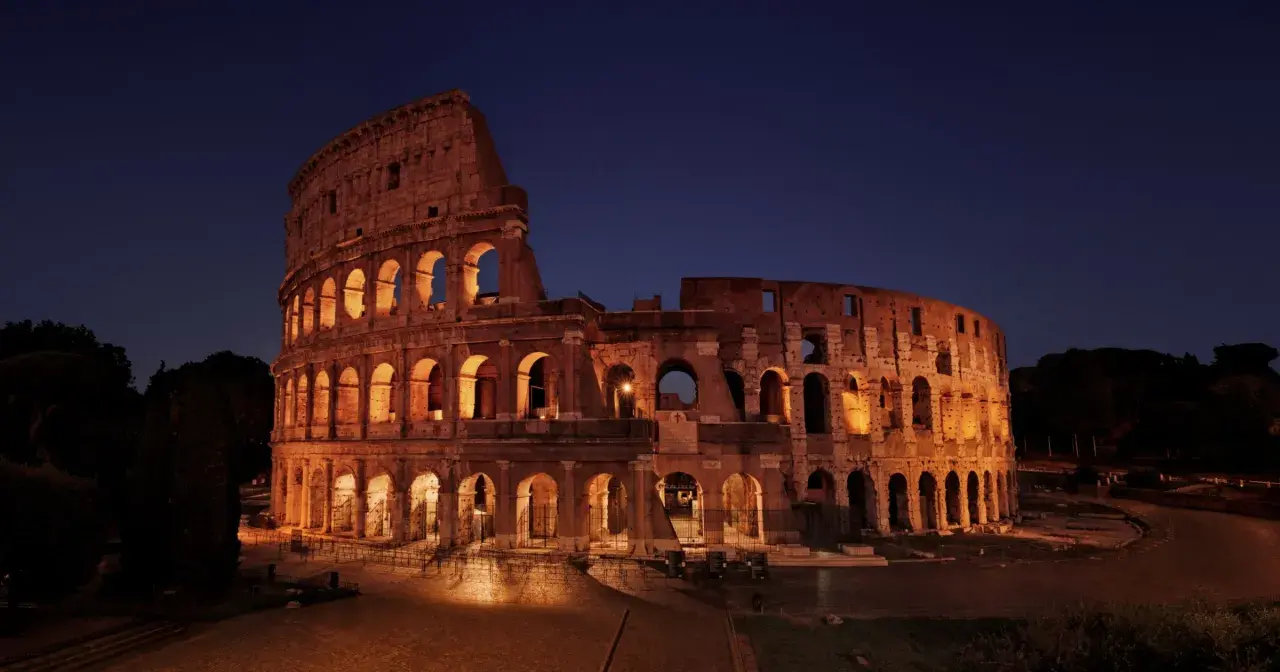 Il Colosseo illuminato di notte, con i suoi archi che creano un gioco di luci e ombre. Ci si chiede perche il Colosseo è bucato, ma la sua storia è scritta nelle sue ferite.