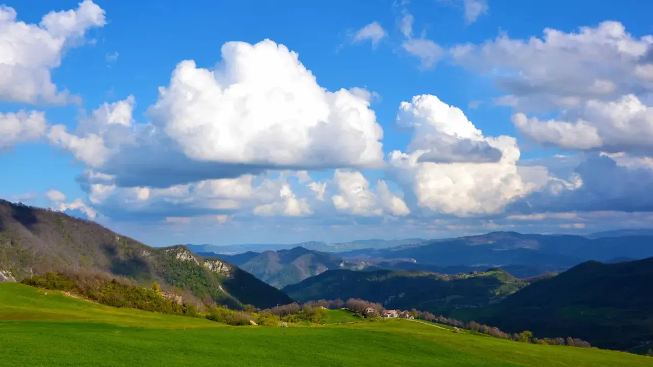 Colli bolognesi cosa vedere: verdi colline, case sparse e un cielo azzurro con nuvole bianche.