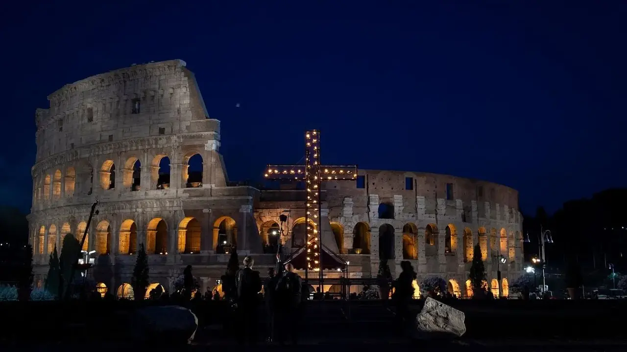 Colosseo illuminato di notte con una croce luminosa, un'atmosfera suggestiva che ricorda quando si festeggia Pasqua.