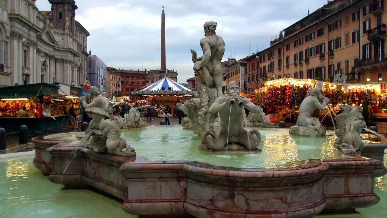 Fontana dei Quattro Fiumi a Piazza Navona, Roma, con bancarelle illuminate che anticipano quando iniziano i mercatini di Natale a Roma.