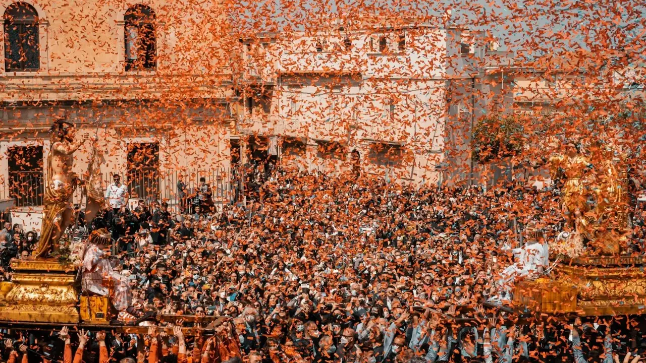 Folla festante sotto una pioggia di coriandoli arancioni, mentre si celebra cosa si festeggia a Pasqua con una processione solenne.