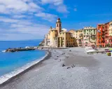 Un mare bello in Liguria, con la spiaggia di ciottoli e le case colorate di Camogli che si affacciano sull'acqua azzurra.