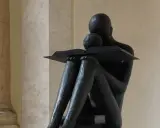 Statua di una figura che legge un libro, con un bambino appoggiato, immersi nella conoscenza a tutto spiano.