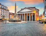 Piazza illuminata con il Pantheon, una chiesa maestosa, e una fontana con obelisco. Tavolini all'aperto invitano a godersi la sera romana.
