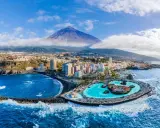 Città costiera con piscina a sfioro e vulcano sullo sfondo. Un'ottima idea su dove andare ad aprile per una vacanza al mare.