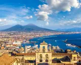 Vista di Napoli con il Vesuvio sullo sfondo, un porto vivace e un campanile antico. Un gioiello tra i siti UNESCO Campania.