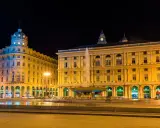 Piazza De Ferrari illuminata di notte, con la fontana centrale e gli edifici storici che animano la vita notturna di Genova.