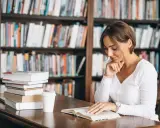 Donna legge in biblioteca, circondata da libri. Il suo studio è un esempio di come l'asindeto, nel significato e negli esempi, arricchisca la narrazione.