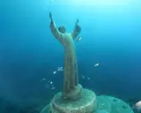 Il Cristo degli Abissi, una statua sommersa, veglia sul fondale blu, circondato da banchi di pesci che nuotano sereni.