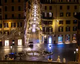 Roma di notte a Natale: una strada illuminata da luci scintillanti, negozi di lusso e una fontana. Un'atmosfera magica per scoprire cosa vedere a Roma a Natale.