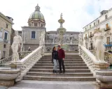 Coppia felice davanti alla Fontana Pretoria, un luogo imperdibile da vedere a Palermo, con le sue statue e la cupola in lontananza.