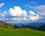 Colli bolognesi cosa vedere: verdi colline, case sparse e un cielo azzurro con nuvole bianche.