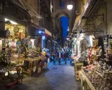 La via di San Gregorio Armeno, Napoli, illuminata di sera, con botteghe artigiane piene di presepi e statuine.