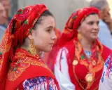 Giovani donne con foulard rossi ricamati e grandi orecchini dorati, un'immagine che evoca la tradizione di fare il portoghese con eleganza.