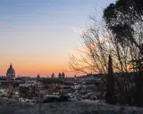 Un magico pincio roma tramonto con cupole che si stagliano contro il cielo aranciato, alberi spogli in primo piano.