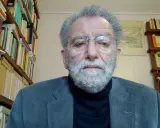 Uomo anziano con barba grigia, occhiali e giacca, circondato da scaffali pieni di libri. Il suo sguardo intenso suggerisce che ei fu significato.