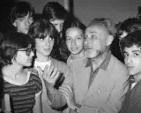 Un uomo anziano con barba e capelli grigi parla animatamente a un gruppo di giovani. Se questo è un uomo riassunto, è un uomo che ispira e coinvolge.