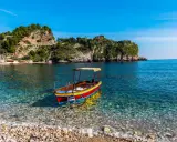 Barca colorata in un mare cristallino, ideale per scoprire cosa fare a Ferragosto in Sicilia, tra scogliere verdi e borghi pittoreschi.