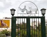 Cancello verde con insegna "FATTORIA" e sagome di animali. A sinistra, murale di un uomo su trono. Danisinni, Palermo.