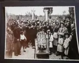 Una folla partecipa a un funerale, con un feretro fiorito al centro. Questa foto post mortem cattura un momento di lutto collettivo.