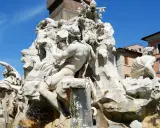 Fontana dei Quattro Fiumi di Bernini in Piazza Navona, Roma. Sculture maestose e acqua zampillante sotto un cielo azzurro.