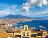Vista panoramica di Napoli città con il Vesuvio sullo sfondo, il porto e un campanile in primo piano.