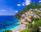 Positano, un gioiello incastonato tra il verde dei monti e l'azzurro del mare in Campania. Case colorate a picco sul mare, una spiaggia affollata e barche che solcano le acque cristalline.