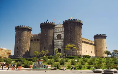 Il maestoso Maschio Angioino di Napoli, con le sue torri imponenti e l'arco trionfale, si staglia contro il cielo azzurro.