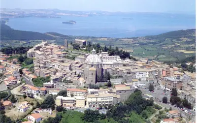 Vista aerea di un borgo italiano con cupola imponente, circondato da case con tetti rossi e affacciato su un lago. Est est est.