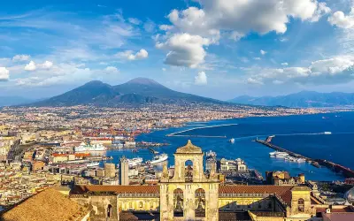 Vista panoramica di Napoli città con il Vesuvio sullo sfondo, il porto e un campanile in primo piano.