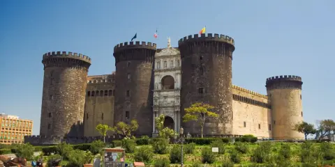 Il maestoso Maschio Angioino di Napoli, con le sue torri imponenti e l'arco trionfale, si staglia contro il cielo azzurro.