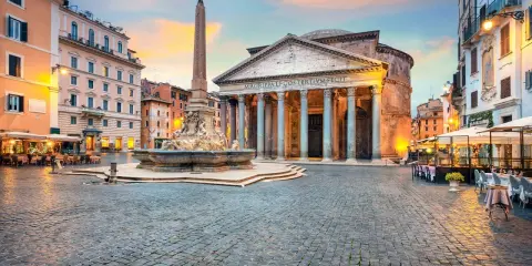 Piazza illuminata con il Pantheon, una chiesa maestosa, e una fontana con obelisco. Tavolini all'aperto invitano a godersi la sera romana.