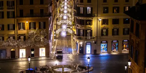 Roma di notte a Natale: una strada illuminata da luci scintillanti, negozi di lusso e una fontana. Un'atmosfera magica per scoprire cosa vedere a Roma a Natale.