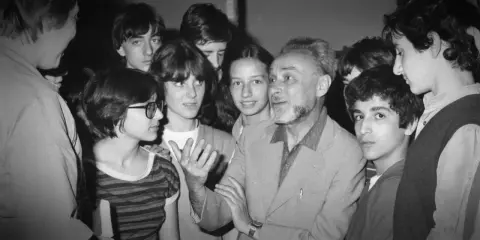 Un uomo anziano con barba e capelli grigi parla animatamente a un gruppo di giovani. Se questo è un uomo riassunto, è un uomo che ispira e coinvolge.