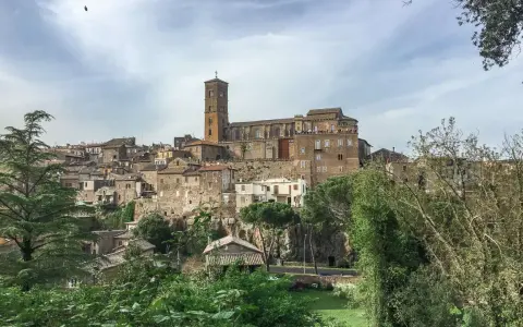 Panoramica dell'antico borgo di Sutri, con le sue case in pietra arroccate su una collina e una maestosa cattedrale con campanile.