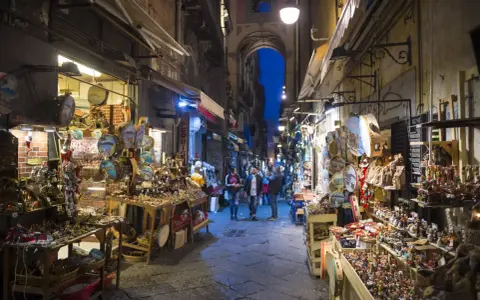 La via di San Gregorio Armeno, Napoli, illuminata di sera, con botteghe artigiane piene di presepi e statuine.