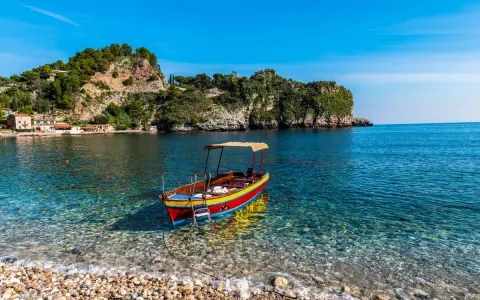 Barca colorata in un mare cristallino, ideale per scoprire cosa fare a Ferragosto in Sicilia, tra scogliere verdi e borghi pittoreschi.