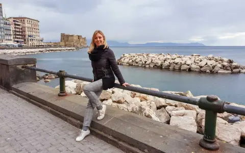Donna sorridente appoggiata a un parapetto con Castel dell'Ovo sullo sfondo, una giornata tipica di napoli a gennaio.