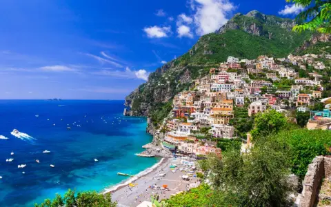 Positano, un gioiello incastonato tra il verde dei monti e l'azzurro del mare in Campania. Case colorate a picco sul mare, una spiaggia affollata e barche che solcano le acque cristalline.