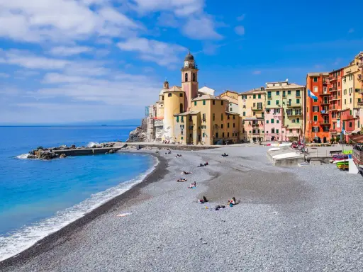 Un mare bello in Liguria, con la spiaggia di ciottoli e le case colorate di Camogli che si affacciano sull'acqua azzurra.