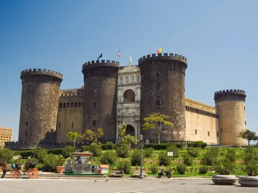 Il maestoso Maschio Angioino di Napoli, con le sue torri imponenti e l'arco trionfale, si staglia contro il cielo azzurro.