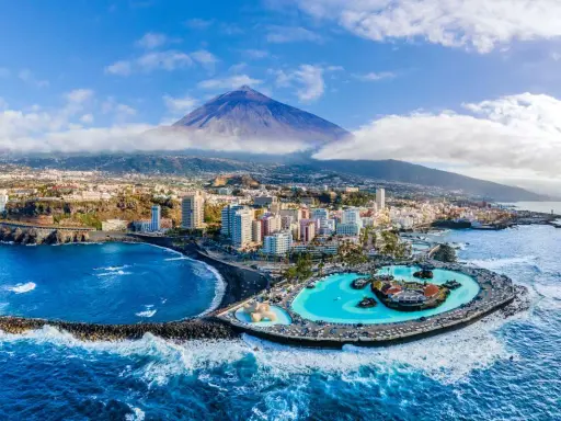 Città costiera con piscina a sfioro e vulcano sullo sfondo. Un'ottima idea su dove andare ad aprile per una vacanza al mare.