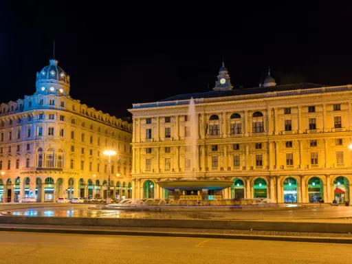Piazza De Ferrari illuminata di notte, con la fontana centrale e gli edifici storici che animano la vita notturna di Genova.