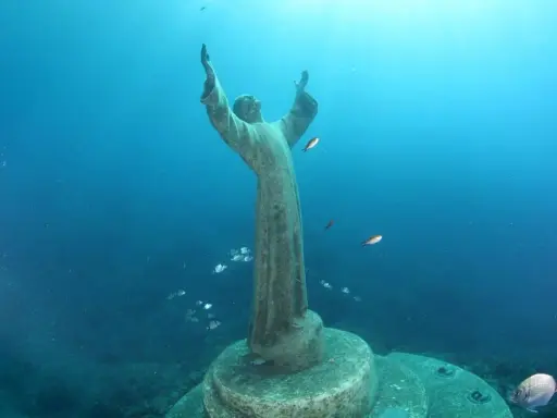 Il Cristo degli Abissi, una statua sommersa, veglia sul fondale blu, circondato da banchi di pesci che nuotano sereni.
