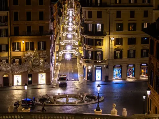 Roma di notte a Natale: una strada illuminata da luci scintillanti, negozi di lusso e una fontana. Un'atmosfera magica per scoprire cosa vedere a Roma a Natale.