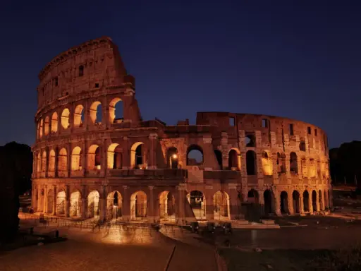 Il Colosseo illuminato di notte, con i suoi archi che creano un gioco di luci e ombre. Ci si chiede perche il Colosseo è bucato, ma la sua storia è scritta nelle sue ferite.